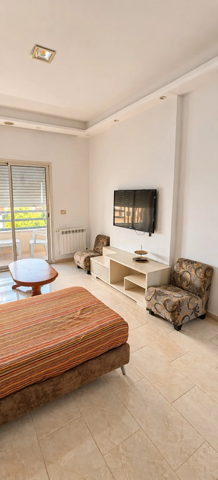 Salon meublé avec télévision et ouverture sur un balcon